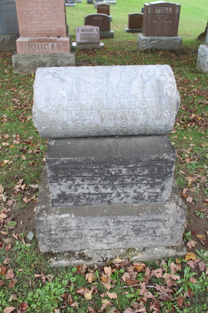 aged stone grave with light grey pillar on top surrounded by other gravestones